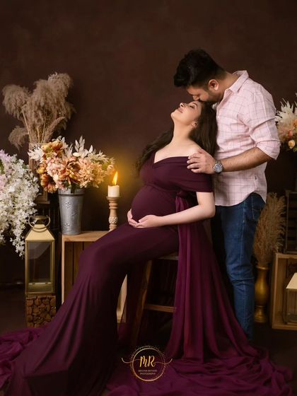 A romantic pose in a candlelit setting. The partner gently kisses his wife's head as she leans back, seated on a stool in an elegant purple gown.