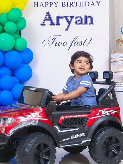"Two Fast!" A car-themed second birthday party for a little boy who loves things that go. The setup includes a custom backdrop, a large number '2' shaped like a racetrack, and a cool ride-on car for the perfect photo opportunity.