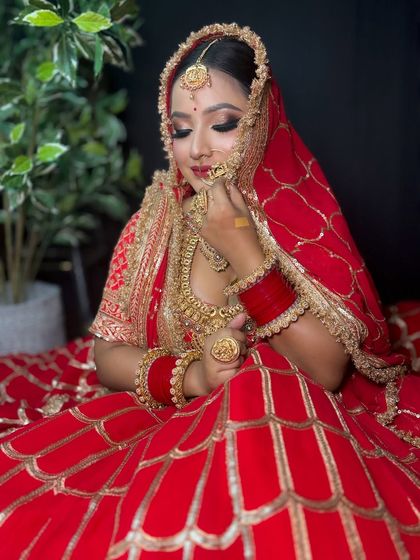 A beautiful shot of a bride in a traditional red lehenga with intricate gold work. Her makeup features a classic smokey eye with a touch of gold glitter and a deep red lip.