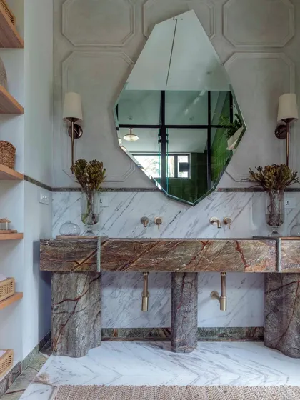 A detail of the master bathroom in Summer Haus, showcasing our passion for material expression. Here, a custom-fabricated vanity from richly veined marble stands as a sculptural element, complemented by a uniquely shaped mirror and artisanal wall sconces.