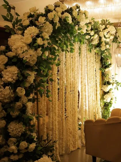 An arch of lush white hydrangeas and roses set against a backdrop of hanging white floral strings (rajnigandha). This combination creates a beautifully fragrant and textured setting.
