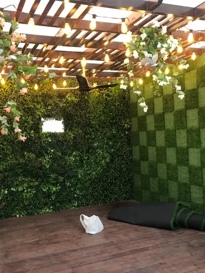 For this pergola in Dilshad Garden, I created a feature wall with a checkerboard pattern using two different tones of artificial grass. The hanging plants and lights complete the cozy atmosphere.