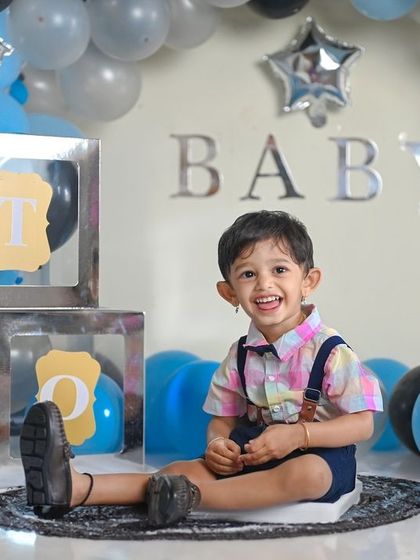 A happy toddler enjoying his second birthday photoshoot. The balloon arch and 'TWO' blocks make the celebration clear.