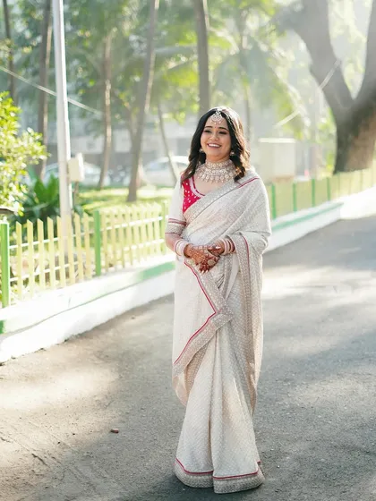 A full-length shot of the bride in an elegant white saree, taking a stroll on a sunlit path. She looks serene, happy, and incredibly graceful.