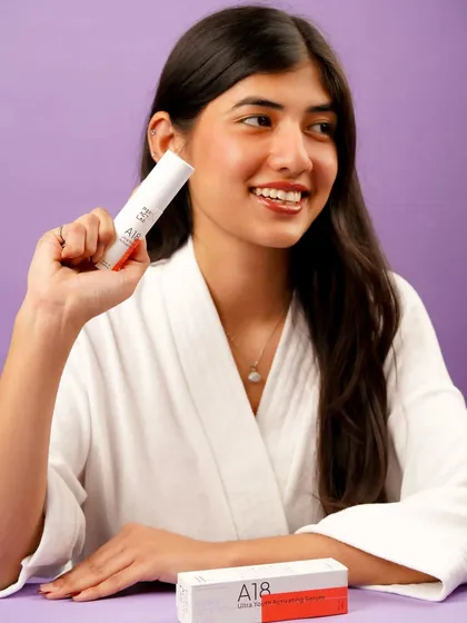 A model in a comfortable white robe holds the product, suggesting a post-shower or spa-like routine. The purple background adds a pop of color while keeping the focus on relaxation and skin health.