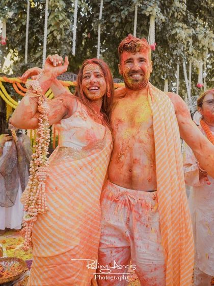 A candid shot of the couple, smeared with haldi and colors, posing happily for the camera. This photo perfectly captures the fun and messy reality of the celebration.