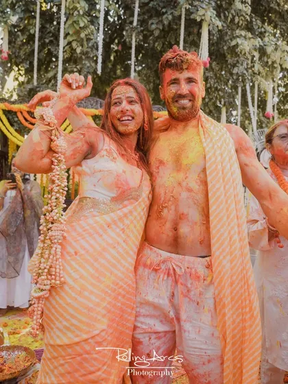 A candid shot of the couple, smeared with haldi and colors, posing happily for the camera. This photo perfectly captures the fun and messy reality of the celebration.