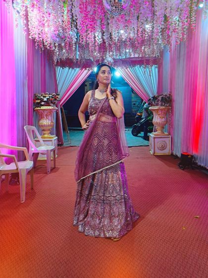 A client posing in a shimmery purple lehenga at a wedding venue, looking glamorous.