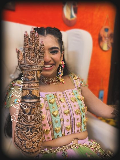 The joy on a bride's face says it all. Here she is, laughing and showing off her intricate full arm mehndi, which is filled with traditional figures and patterns for her special day.