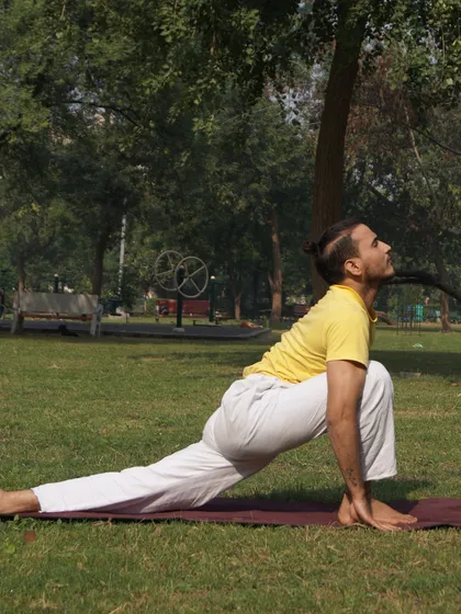 A student practices Ashwa Sanchalanasana (Equestrian Pose) outdoors, connecting the practice of yoga with the tranquility of nature.