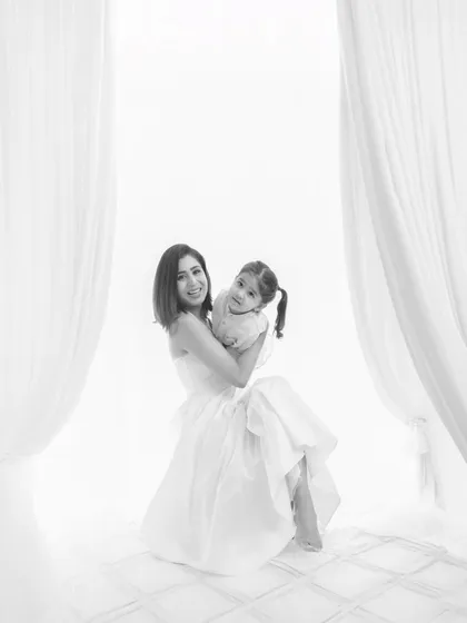 A joyful black and white portrait of a mother holding her daughter. The high-key lighting and white background create a classic, timeless look, while their bright smiles radiate pure happiness and love.