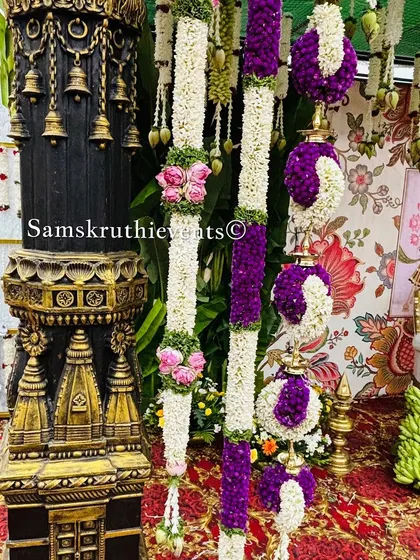 A detailed view of traditional decor elements, including a miniature temple pillar and hanging floral arrangements made of jasmine and purple flowers.