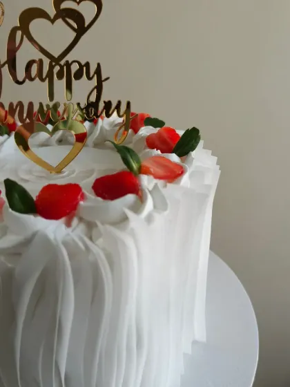 A closer look at the details on the white anniversary cake. The combination of crisp white frosting and vibrant red strawberries makes it a stunning centerpiece.
