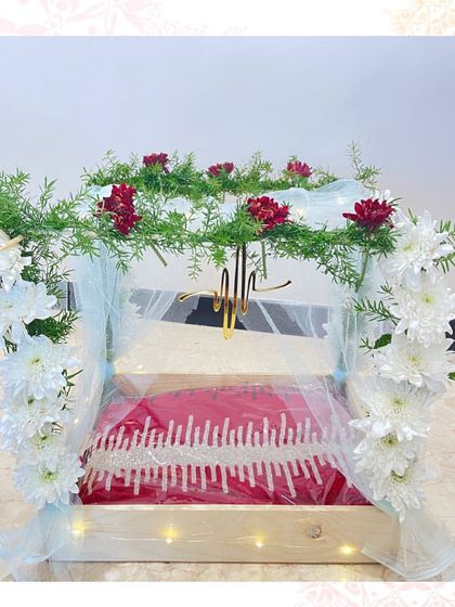 A simple and elegant trousseau tray for a red garment, framed by a delicate arch of fresh flowers and greenery, lit from below to create a warm glow.
