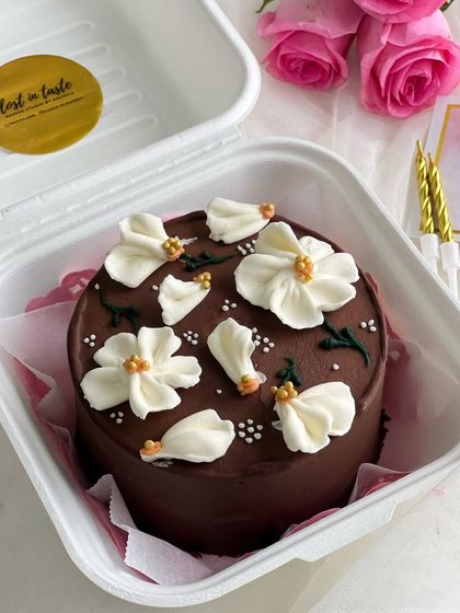 An elegant Belgian chocolate bento cake decorated with delicate, hand-piped white buttercream flowers. The contrast between the dark chocolate and the white florals is timeless.