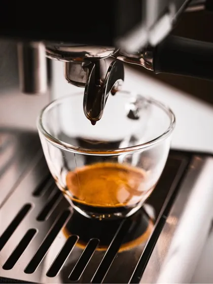 A close-up of an espresso shot being pulled. The focus on the rich, dark liquid and the metallic sheen of the machine creates a powerful, professional image.
