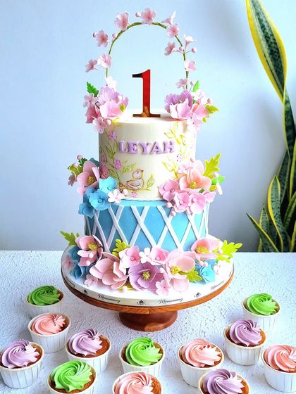 An enchanted garden cake with a blue and pink color scheme. This two-tiered cake is covered in handmade sugar flowers and features a delicate floral hoop topper.