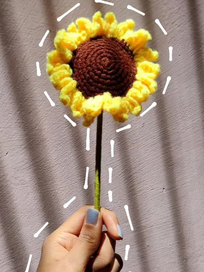 A single crochet sunflower held up, with graphic lines emphasizing its shape.