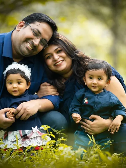 A beautiful family portrait taken outdoors in a lush, green park. The natural setting adds a warm and vibrant feel to the photo.