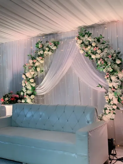 A simple yet stunning nikah or engagement stage. The design is built around a graceful arch of white and pink roses against a backdrop of soft white drapes and fairy lights.