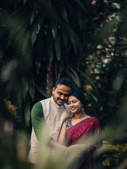 A loving couple framed by lush green foliage in a park. This style of portrait uses natural surroundings to create a sense of intimacy and seclusion.
