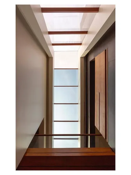 The staircase in the "House with Parallel Planes" is located within a light-filled atrium. A continuous skylight above bathes the teakwood stairs in natural light.