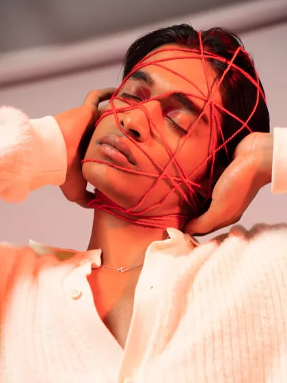 A high-concept editorial look for a male model. The makeup is clean and subtle, allowing the creative prop of the red thread to be the main focus of the image.