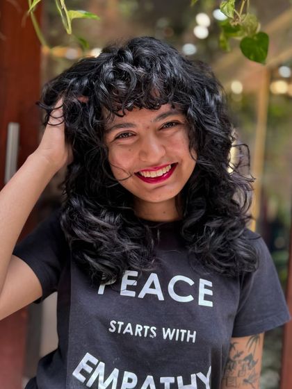 Curly bangs are the cutest! This client is radiating joy with her new fringe and layered cut that perfectly frames her smiling face.