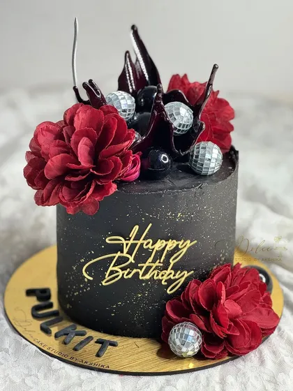 A bold and beautiful black birthday cake. This design is decorated with deep red flowers, chocolate sails, and silver disco balls for a touch of party glamour.