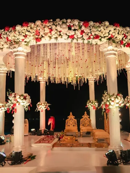 A classic round mandap with white pillars and a canopy of red and white flowers, perfect for a timeless and elegant night-time wedding ceremony.