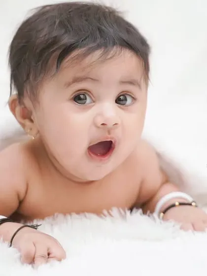 A surprised and adorable expression from a three-month-old peeking out from under a blanket.