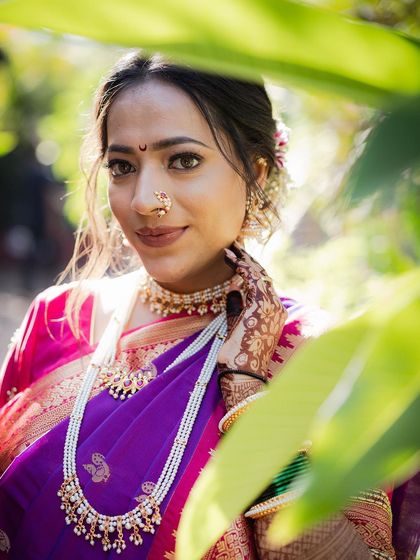 A classic bridal portrait framed by green leaves. The bride looks directly at the camera, her gentle smile and traditional Maharashtrian jewelry creating a timeless and beautiful image.