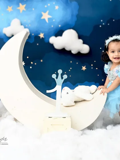 A "love you to the moon and back" themed photoshoot. This little girl in her pretty blue dress looks right at home among the stars and clouds.