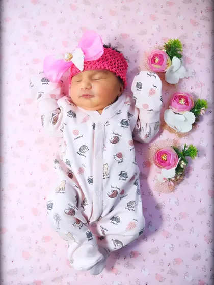 A peaceful baby girl in a pink knitted headband and a cute printed onesie, sleeping soundly.