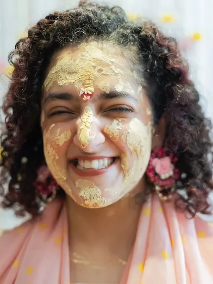 The pure, unadulterated joy of a Haldi ceremony. This close-up captures the bride's infectious smile amidst the playful chaos, a moment of pure happiness that radiates warmth and love.