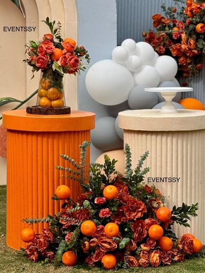 A close-up of the decor elements, including a vase filled with oranges and roses, and floral arrangements featuring real santras. These small details are what make a theme feel complete and special.