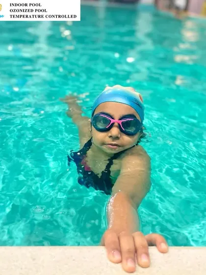 A young swimmer confidently holds onto the edge of the pool. Our coaching helps build strength and technique from the very beginning.