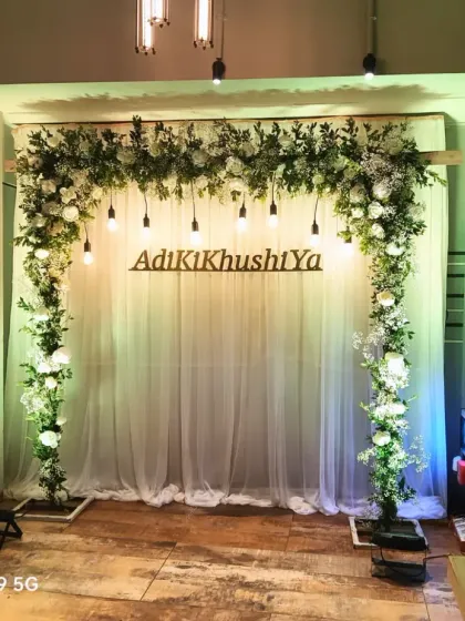 A fresh and simple engagement backdrop with a white floral and greenery arch. The couple's hashtag, "AdiKiKhushiYa," is displayed in the center for a personal touch.