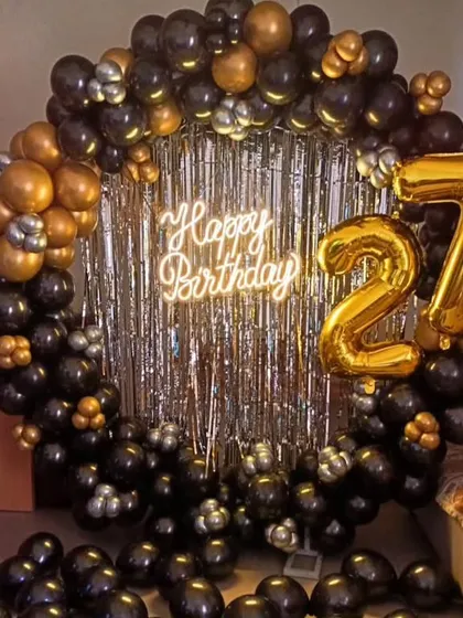 A bold and stylish 27th birthday setup. We created a full ring backdrop with black and gold balloons, a silver shimmer curtain, a neon sign, and large number foil balloons.