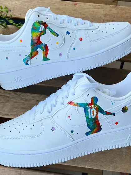 A vibrant, abstract take on sports. These custom Nike AF1s feature colorful silhouettes of a cricketer and a football player, surrounded by paint splatters.