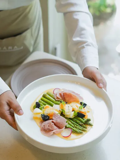 Our chef presents a signature summer dish featuring Himalayan asparagus. This plate highlights our philosophy of using the freshest seasonal produce, served with traditional hollandaise sauce and prosciutto for an elegant dining experience.