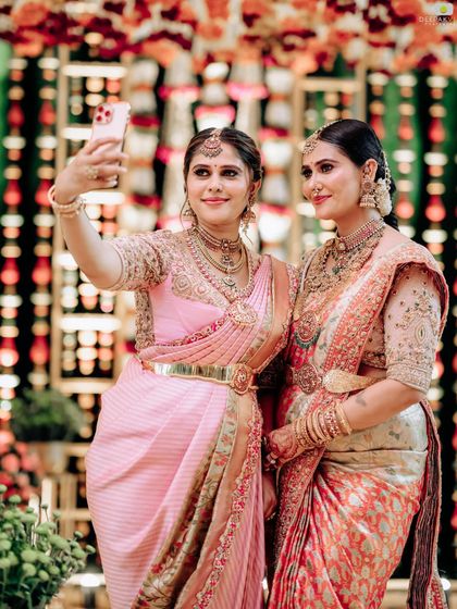 A modern moment in a traditional setting. The sisters take a selfie, capturing their beautiful custom sarees and the festive atmosphere.
