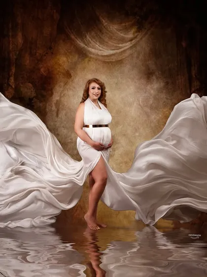 A stunning symmetrical composition with a white gown's fabric flowing out like wings. The swan props and water reflection complete this magical, fairytale-inspired maternity scene.