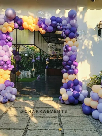 A grand entrance for a butterfly-themed Rice Ceremony. The lush balloon arch in shades of purple and peach creates a stunning entryway for guests.