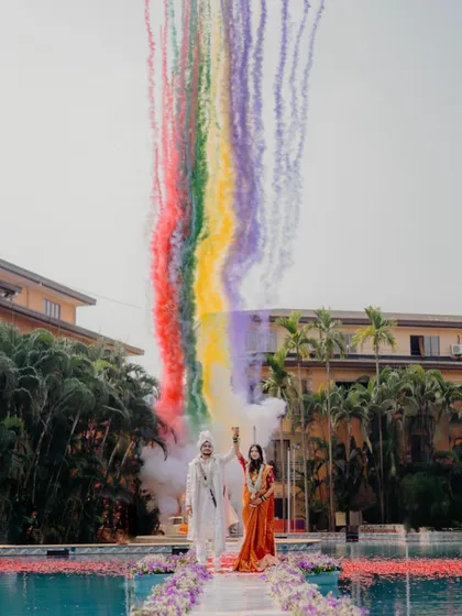 A spectacular wedding moment by the pool with colorful smoke effects. The bride looks stunning in a unique orange-hued saree, showing a modern twist on wedding attire.