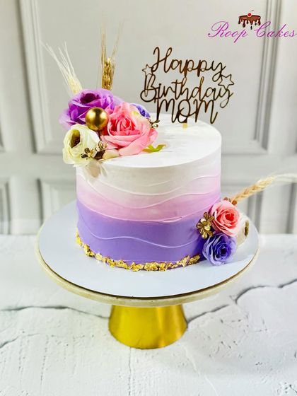 A beautiful birthday cake for Mom, featuring a lovely ombre of purple and pink, adorned with fresh flowers.