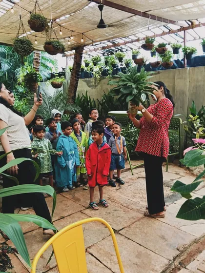 An instructor showing a beautiful plant to a group of children during a nature workshop. Our goal is to spark a lifelong love for gardening and the environment from a young age.