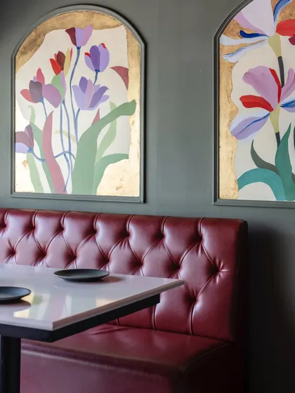 Two arched floral murals seen in their restaurant setting, complementing the rich red of the tufted leather booth. The gold leaf catches the light, creating a warm and inviting atmosphere.