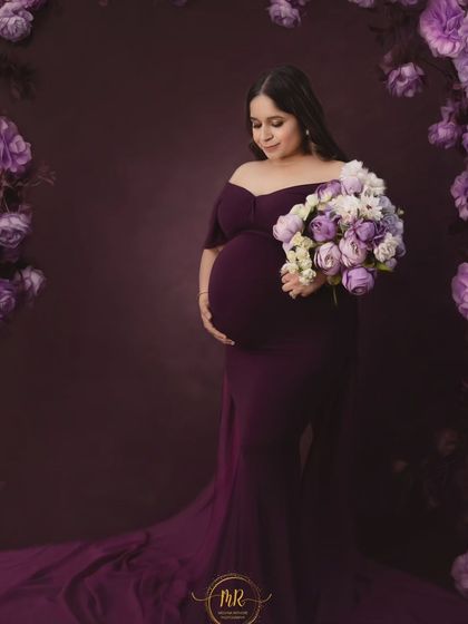 A serene solo portrait with a floral theme. The mother-to-be holds a bouquet of purple and white flowers that perfectly complements her elegant purple gown.