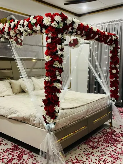 A closer look at one of my signature floral canopy beds. I used a bold combination of red and white faux flowers to create a striking frame, draped with sheer fabric and fairy lights for a warm, inviting glow.
